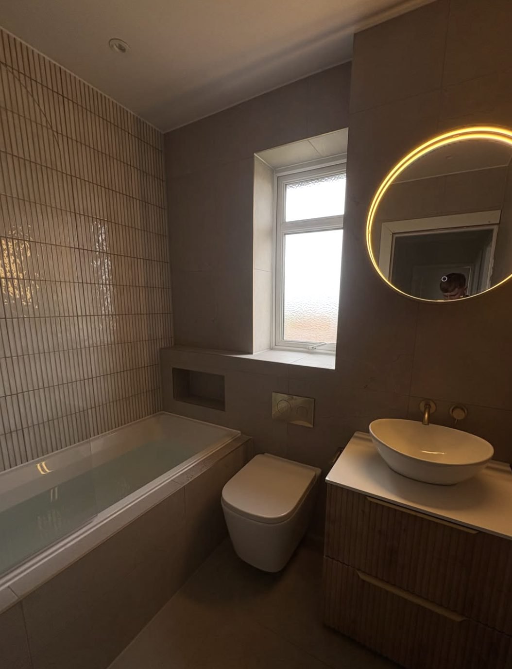 Bathroom with fluted wall tiles, wall hung WC, vessel basin and round backlit mirror